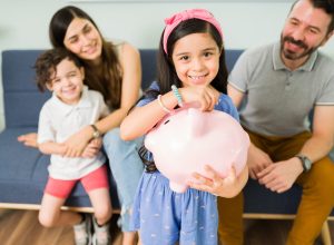 Portrait of a cute little girl putting money on a pink piggy bank to save for a new toy for her and her small brother